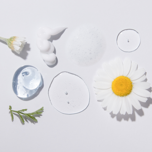 Various skincare serums and creams on a white background next to a daisy